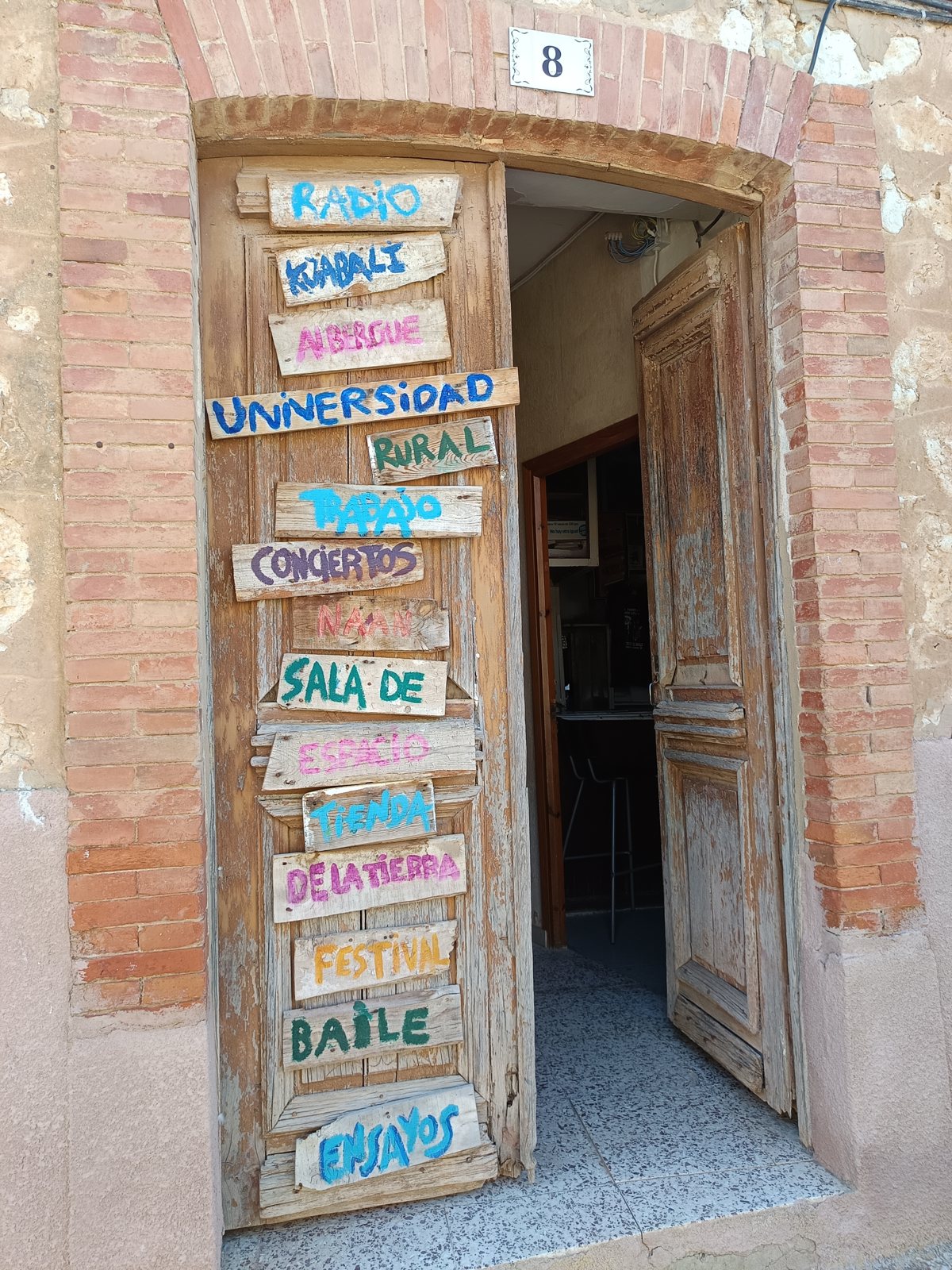 Puerta de la Universidad Rural del Cerrato con sus carteles pintados a mano: radio, albergue, universidad rural, conciertos, sala de ensayo, tienda de la tierra, festival, baile.